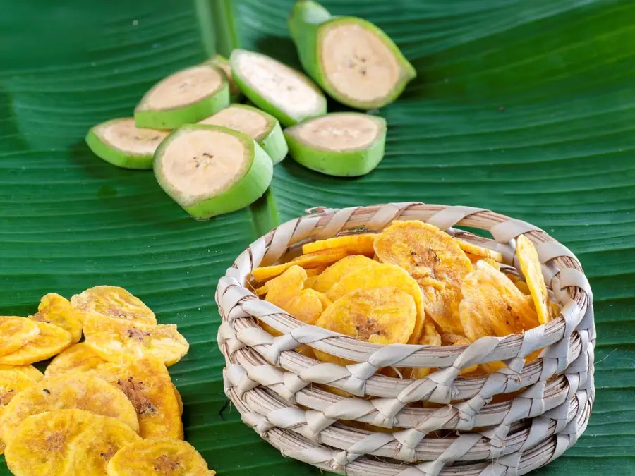 Sliced green plantain and Frittas plantain chips in a basket on a banana leaf