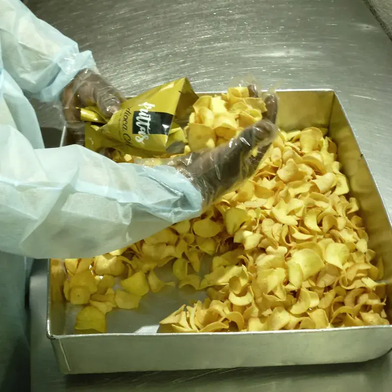 Gloved hands filling a Frittas bag with cassava chips