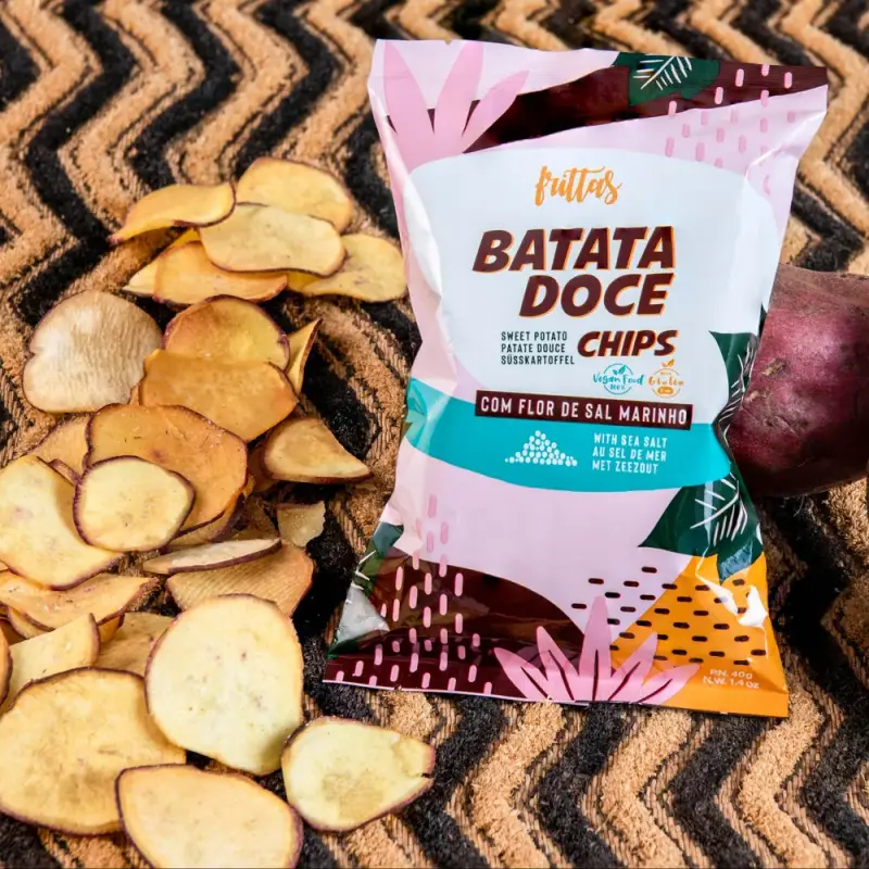 Bag of Frittas sweet potato chips with chips and a raw sweet potato, on a striped mat