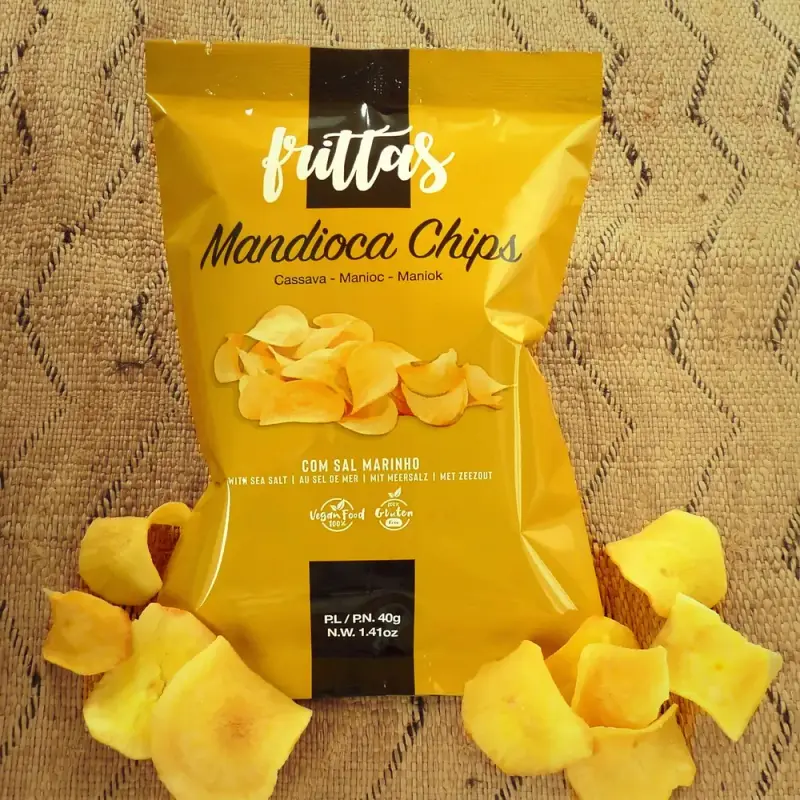 Bag of Frittas cassava chips surrounded by loose chips, on a woven mat